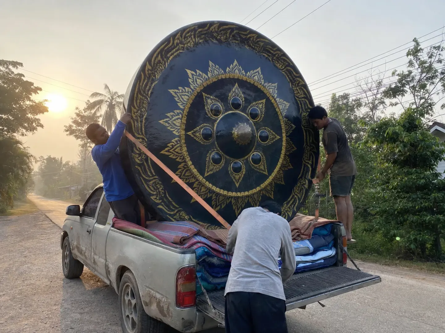 Three people strapping a giant black-and-gold gong upright in a pickup truck bed