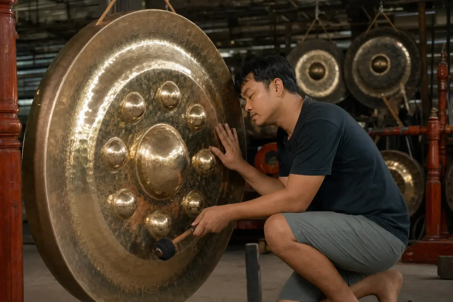 A maker leaning close to a large bossed gong while holding a mallet
